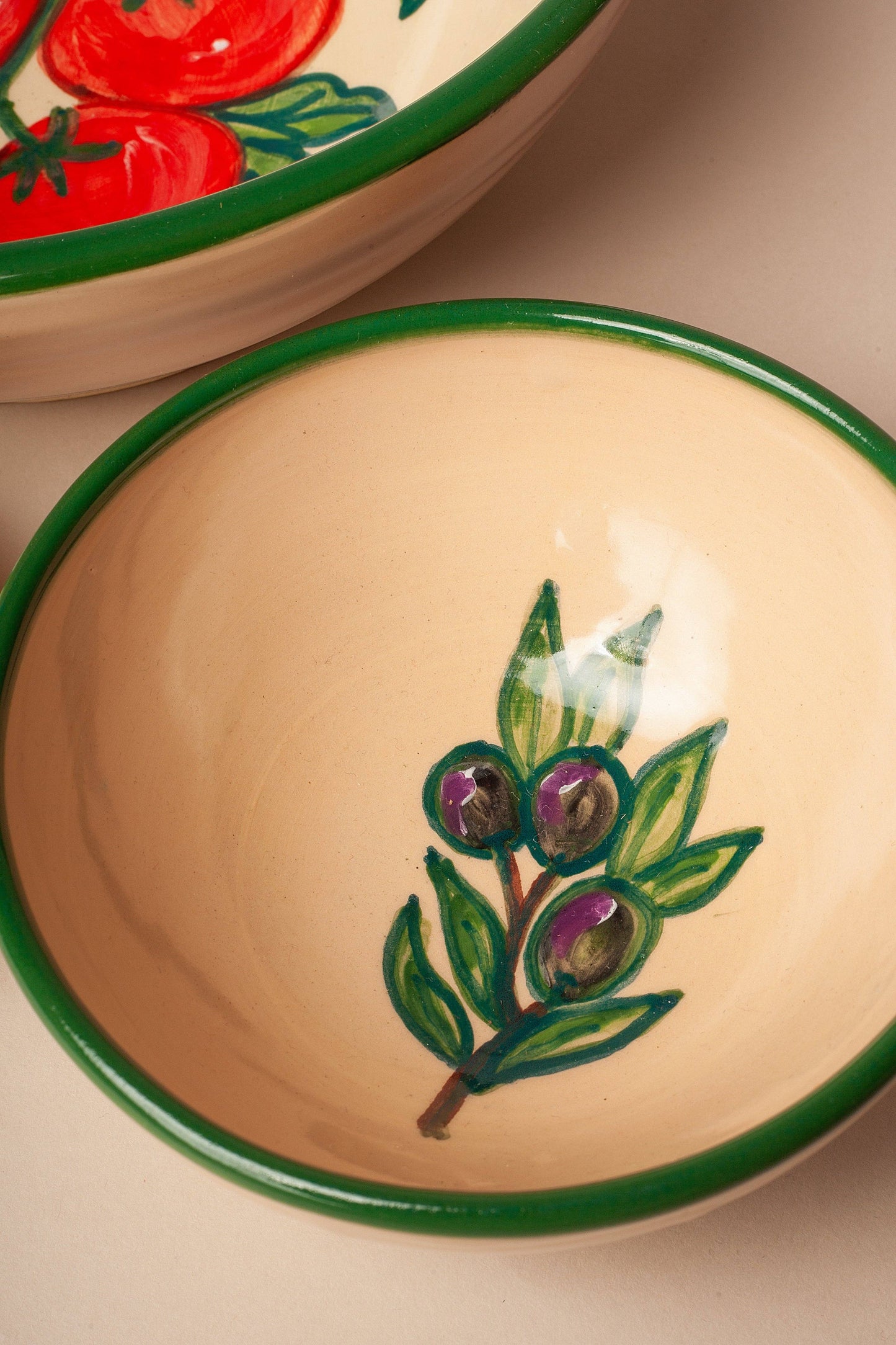 The Huerta Stamped Ceramic Bowl by Eturel Madrid features a green rim and hand-painted olives and leaves, showcasing rustic artisanal charm. Handmade in Spain, it pairs beautifully with bowls displaying red tomatoes.