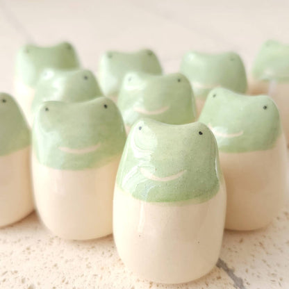 The Little Frog Amulet of Adventures by Picuru ceramicas is a handmade ceramic figurine with a light green top, cream bottom, and dot eyes—a unique gift and joyful symbol of new experiences.
