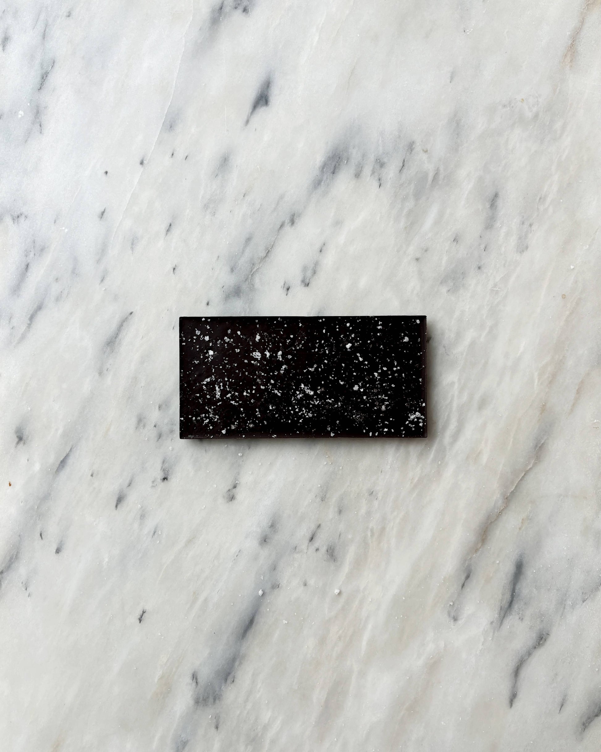 A bar of O Melhor do Ribatejo Dark Chocolate with Flor de Sal rests on a white marble surface veined with gray.