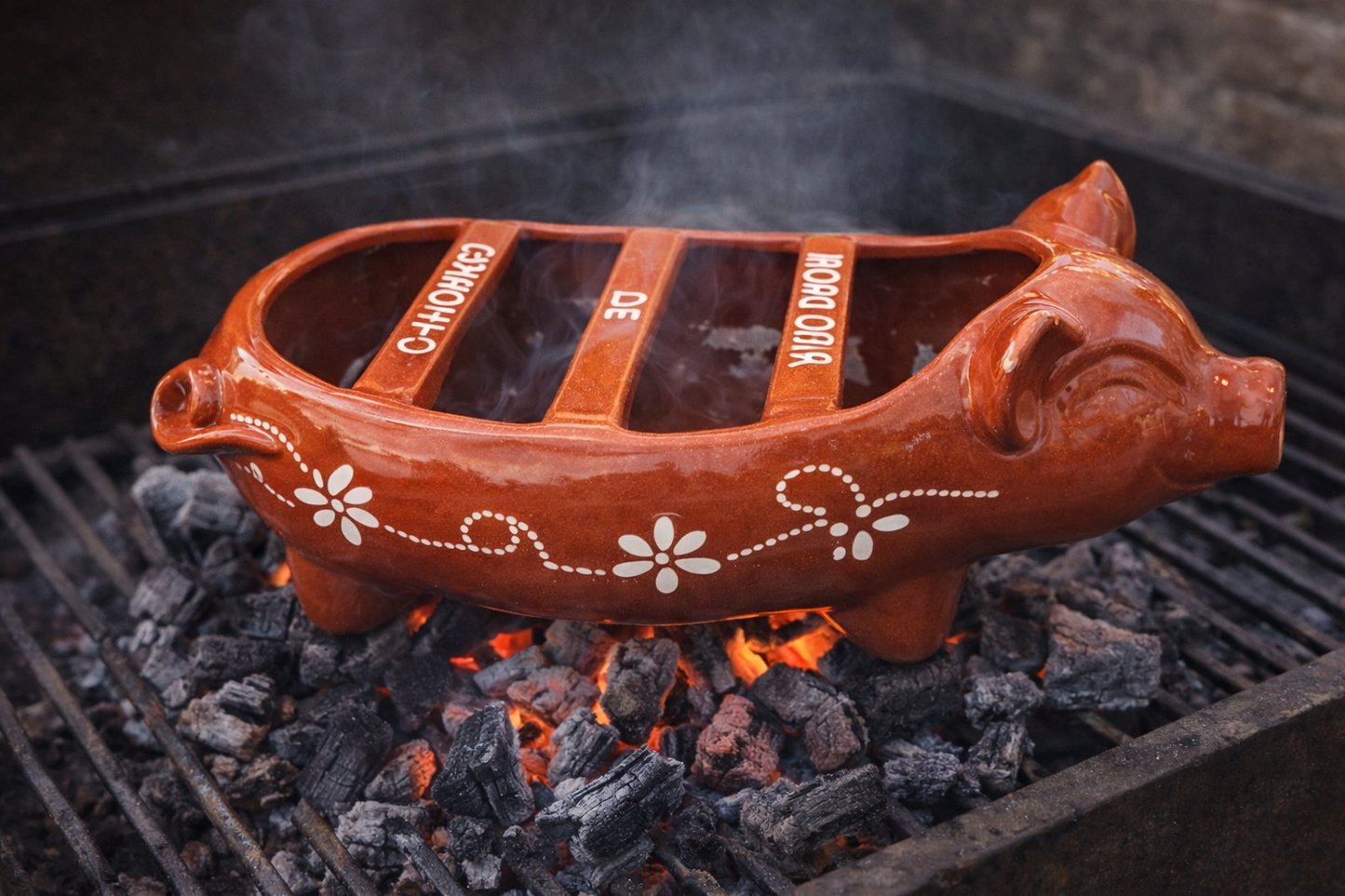 The Ceramica Picas Chorizo Pig Griller Dish, shaped like a pig with divided sections for meats such as smoked sausage, sits over hot coals as steam rises from the terracotta grill.
