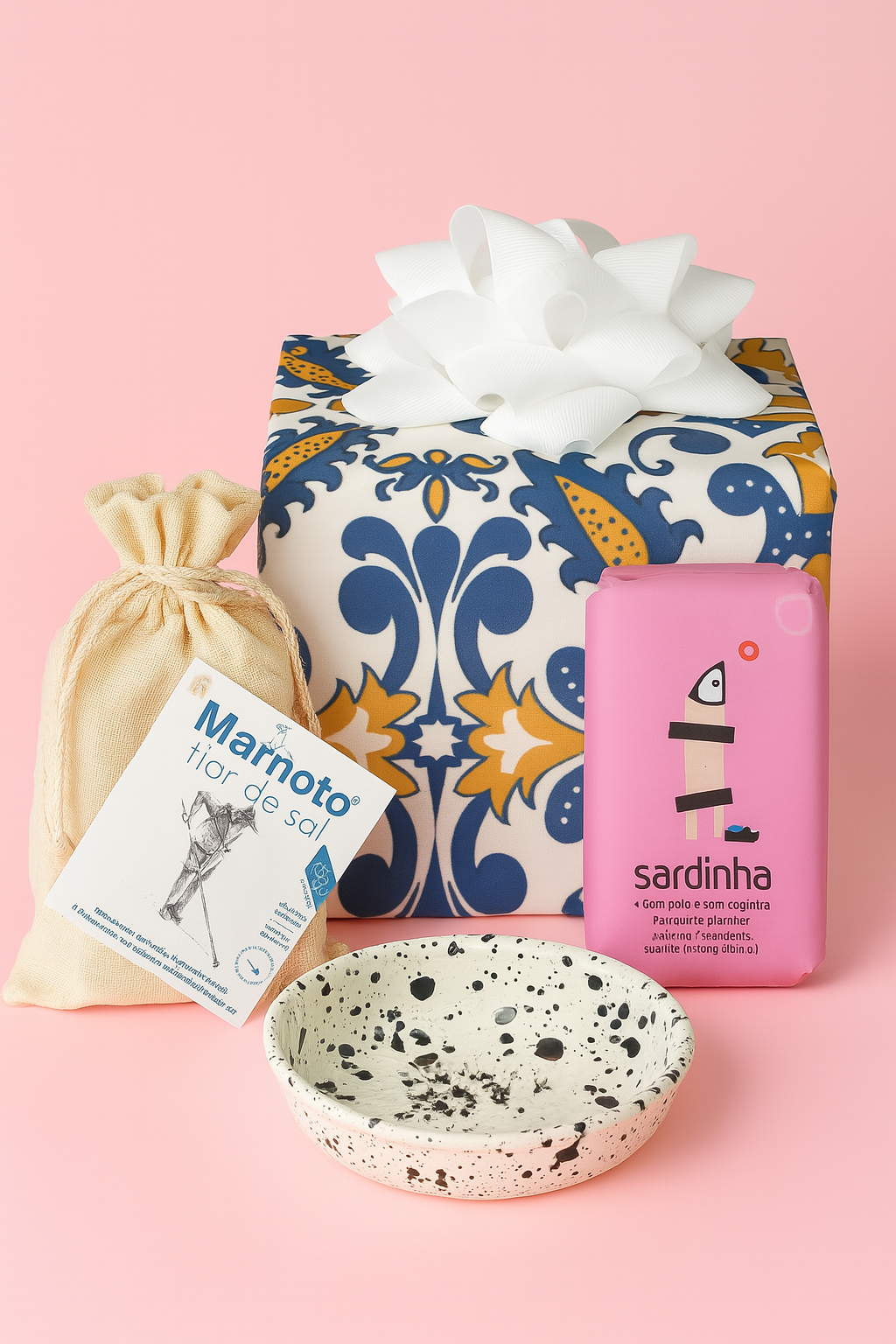 The Iberian sampler kit - Galaxy by Iberica (Pretty things from Portugal) features a wrapped box with a white bow, drawstring pouch, speckled ceramic bowl, Flor de Sal salt flakes, and a pink sardine tin—all on a pink background.