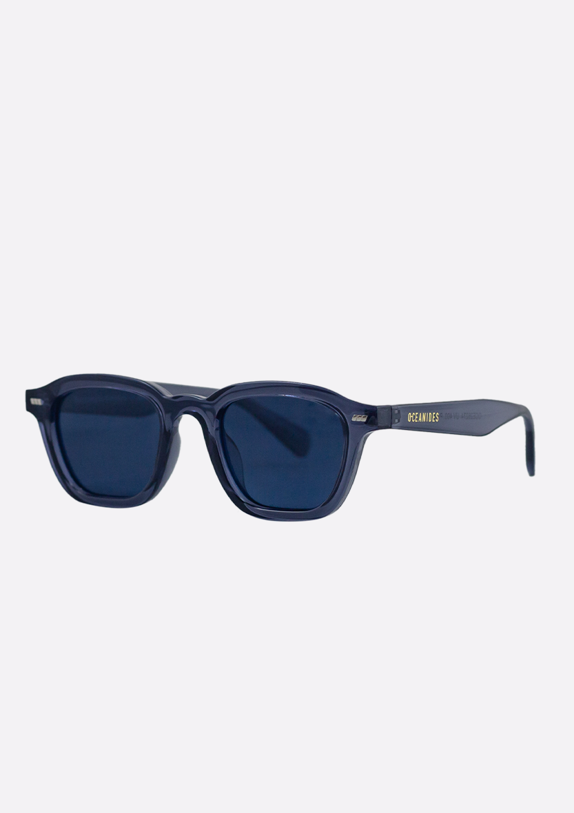 The Neda Crystal Blue Sunglasses by Oceanides feature a navy rectangular recycled plastic frame, polarized lenses, a small gold logo, and "OCEANVUS" on the glossy temple in a modern, minimalist design.