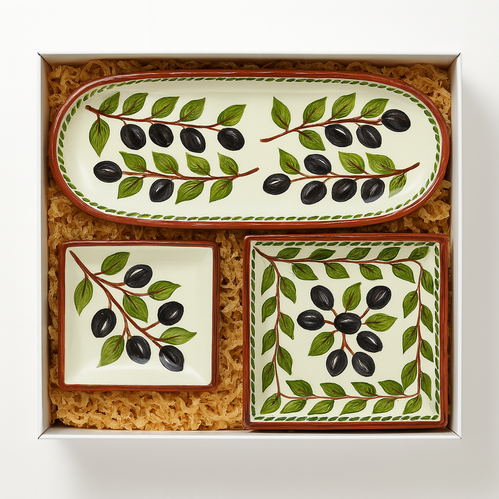 The Iberica Olives serving set, by Pretty things from Portugal, includes three hand-painted ceramic dishes—a rectangular tray and two square plates—nestled in shredded packing material, perfect as a beautiful gift box.