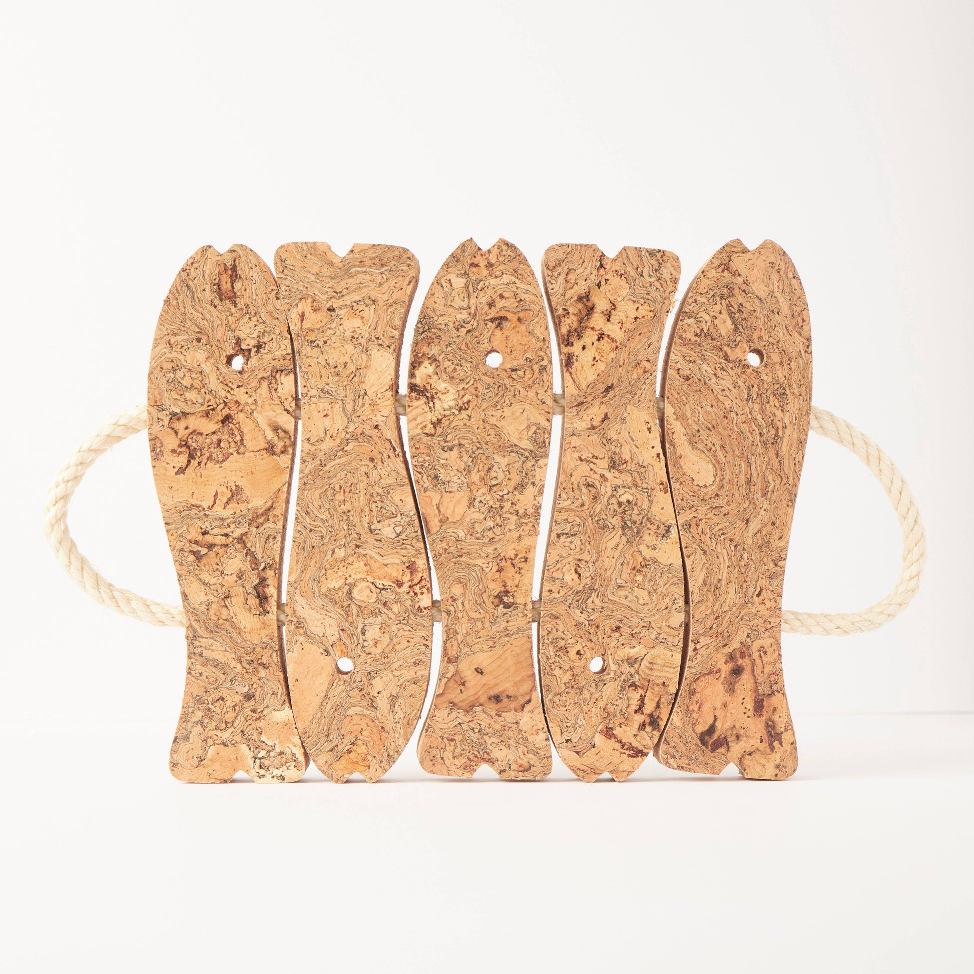 The LIGA Natural Cork Trivet - Fish is an eco cork trivet made of five fish-shaped pieces connected with holes and white rope handles at each end. Crafted in Portugal, it sits on a plain white background.