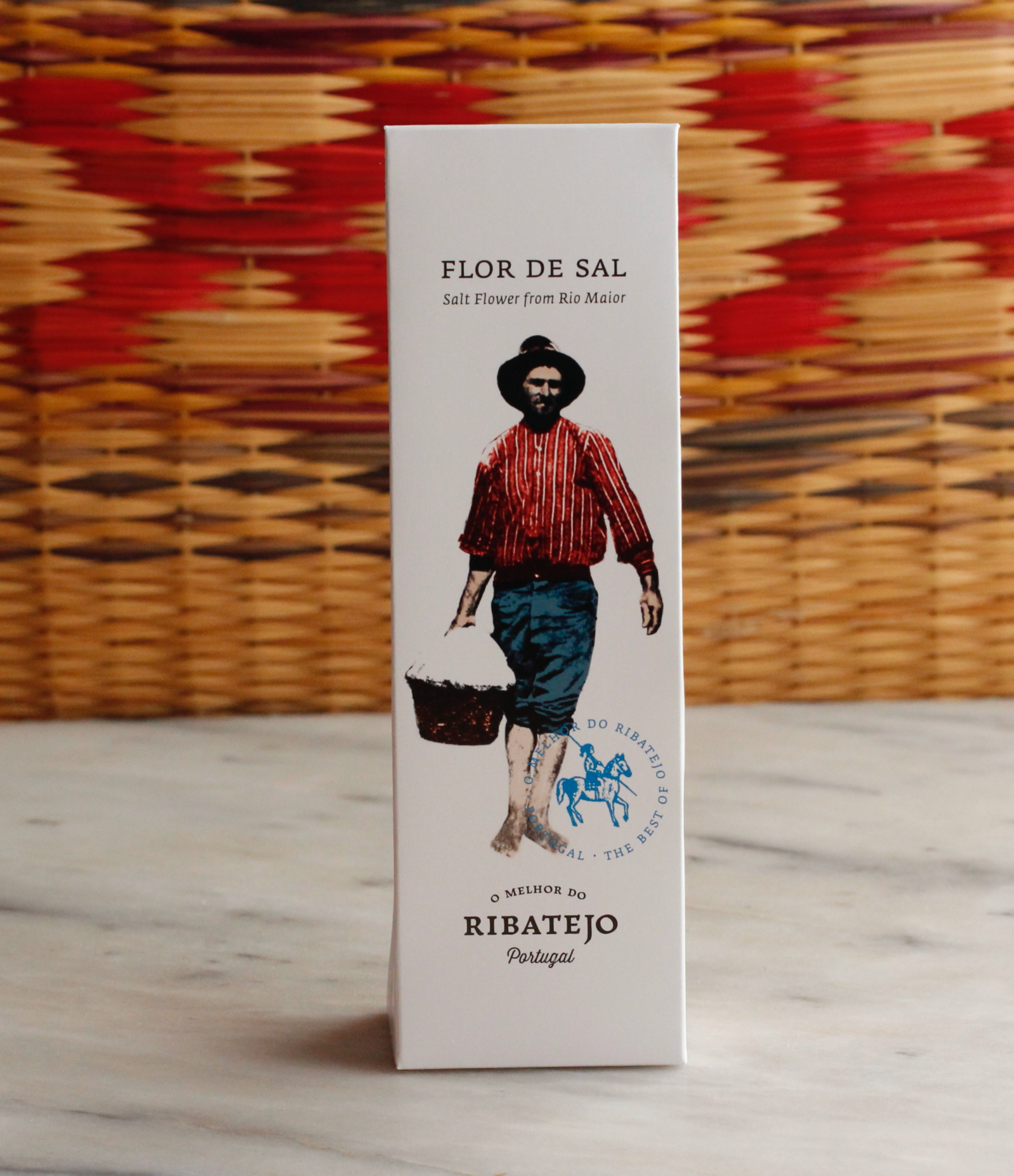 A white box of O Melhor do Ribatejo Salt Flower | From Portugal, featuring an illustration of a person in traditional clothing with a basket, set against a woven basket background.