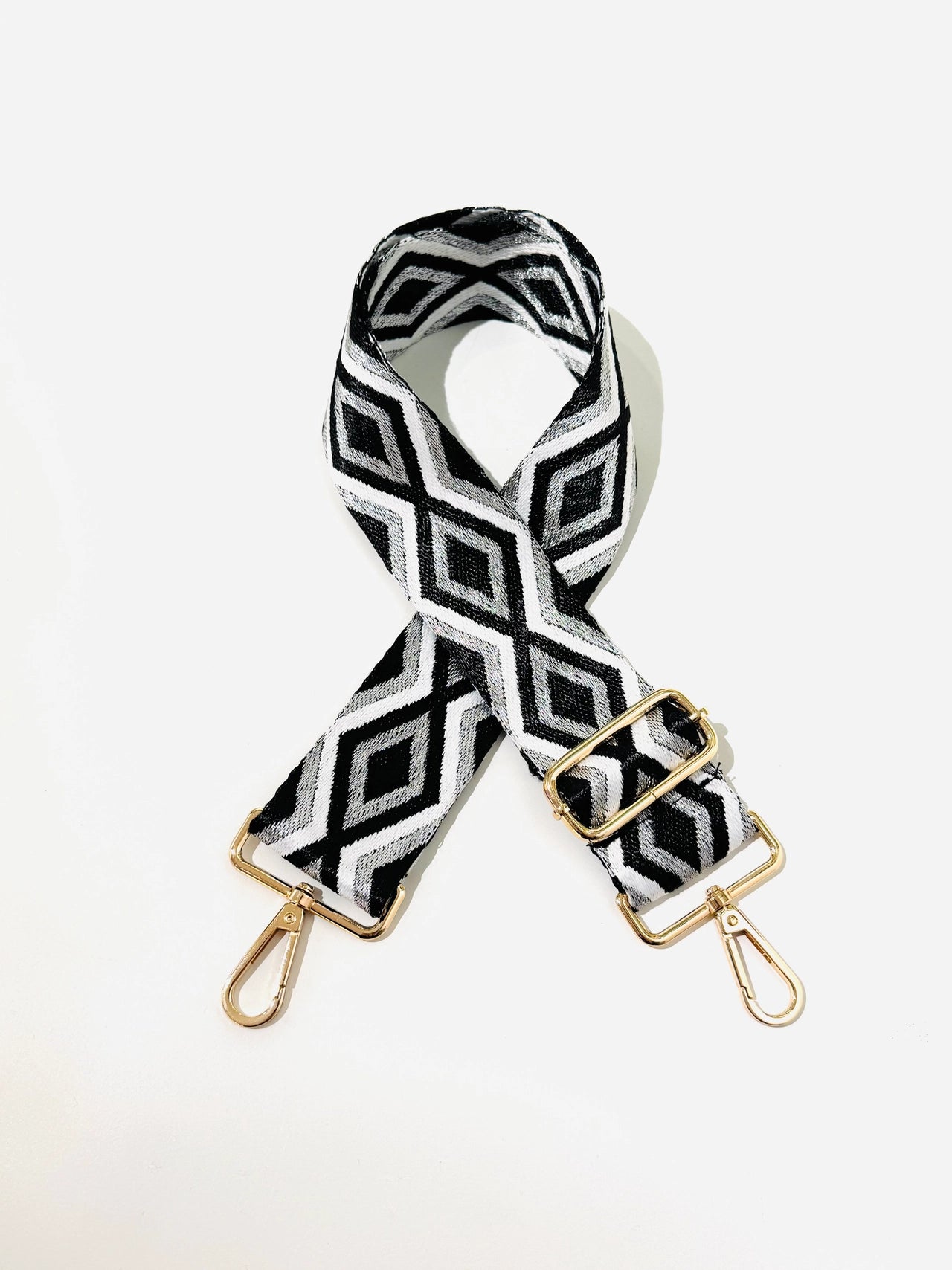 Black and white patterned bag strap with gold hardware on a white background