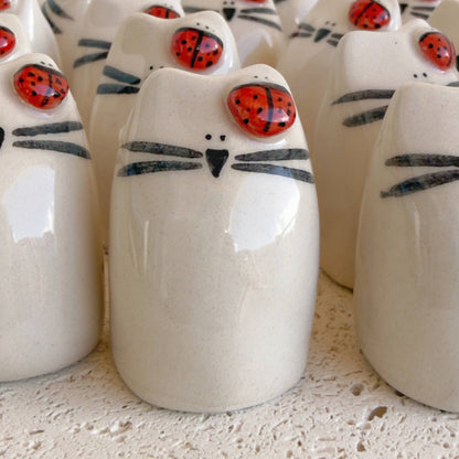 Picuru ceramicas’ Ladybug Amulet, Guardian of Your Dreams – Handmade Lucky Charm Gift features cat-shaped ceramic figurines with black whiskers, a black nose, and a red ladybug on each head, displayed together on a textured white surface.