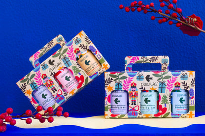 Two festive gift boxes with floral designs hold three bottles each, labeled “Christmas Tea Box | Criatura X Teresa Rego - Special Edition” by Criatura. Red berries and leaves accent the scene—an ideal organic herbal tea gift for the holidays.