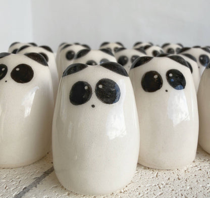 A collection of Picuru ceramicas’ Panda Amulet of Inner Peace – Handmade Lucky Charm Gifts, featuring smooth white ceramic figures with black eyes and spots, is arranged closely on a textured white surface.