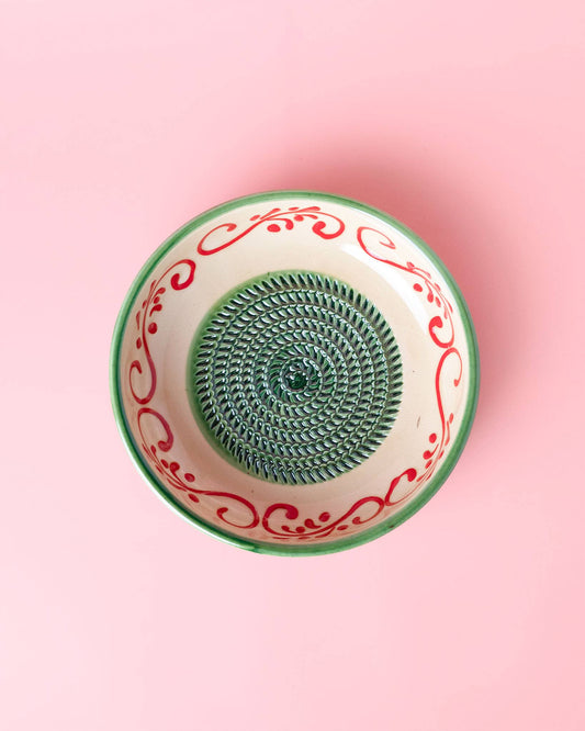 The Alhambra Grater Bowl - Large by Alfar Tierra Cocida is a handcrafted Spanish ceramic piece with an Alhambra-inspired red and green rim, a spiral textured center, and a pastel pink background.