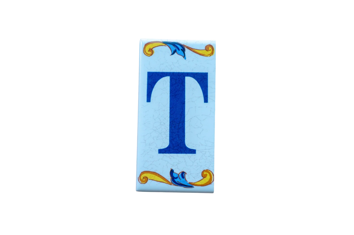 Lisa Croquets Letters – Ceramic House Letter Tiles: rectangular light blue tile featuring a dark blue T with decorative gold and blue scrollwork at the top and bottom.