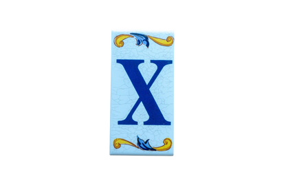 Lisa Croquets Letters – Ceramic House Letter Tiles rectangular tile featuring a blue letter X on a light blue background, accented by decorative yellow and blue scrolls at the top and bottom.