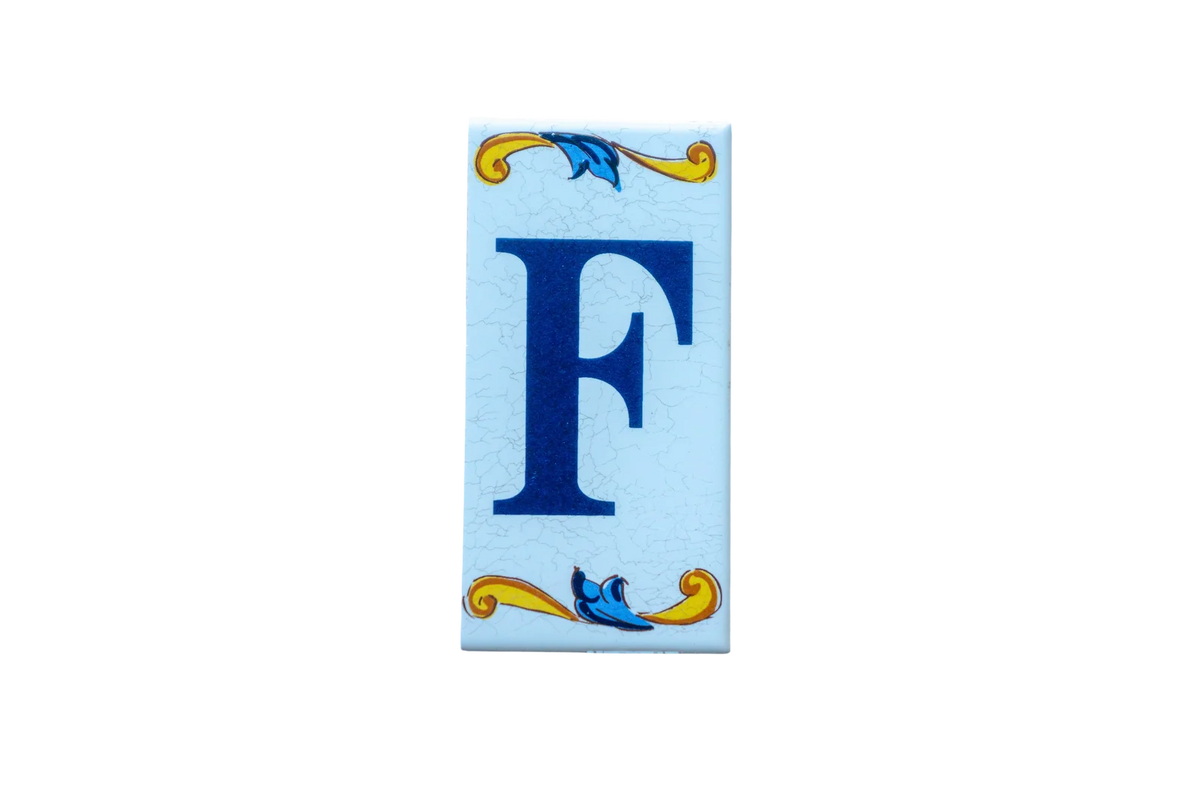 Lisa Croquets Letters – Ceramic House Letter Tiles: a rectangular Spanish ceramic tile featuring the blue letter F decorated with yellow and blue scrollwork at the top and bottom.