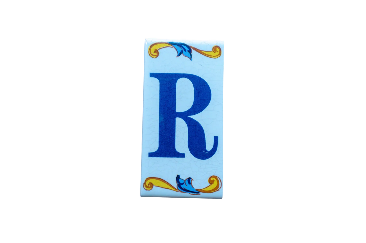 Lisa Croquets Letters – Ceramic House Letter Tiles rectangular Spanish ceramic tile featuring a blue letter R, decorated with blue and yellow scrollwork at the top and bottom.