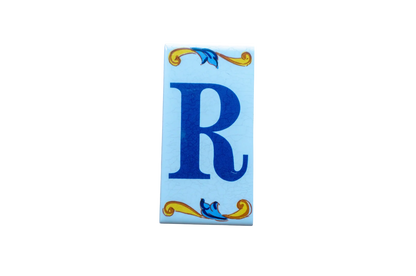 Lisa Croquets Letters – Ceramic House Letter Tiles rectangular Spanish ceramic tile featuring a blue letter R, decorated with blue and yellow scrollwork at the top and bottom.