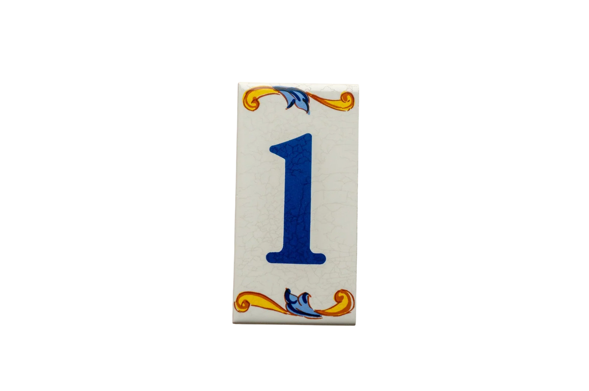 Lisa Croquets Numbers – Ceramic House Number Tiles, handcrafted in Spain, feature the number one in blue on a rectangular tile with yellow and blue scrollwork at the top and bottom.