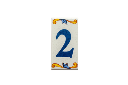 Lisa Croquets Numbers – Ceramic House Number Tiles: rectangular ceramic tile featuring a blue number 2, handcrafted in Spain with decorative yellow and blue scrolls at the top and bottom.