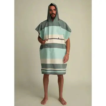 A man stands barefoot, wearing the Futah Papua Adult Beach Poncho – a premium Portuguese cotton surf poncho featuring a hood, short sleeves, and wide horizontal stripes in shades of green, gray, and white. He faces forward against a plain light background.