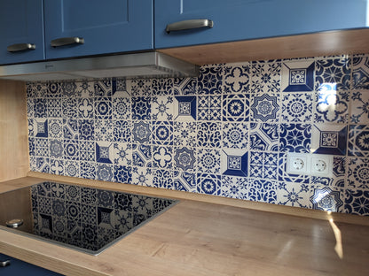 A modern kitchen featuring blue cabinets, a wooden countertop, a black electric stove, and a TilePassion Hand Painted Splashback Set of Azulejo Tiles with blue and white patterns. Two electrical outlets are on the right side of the splashback.